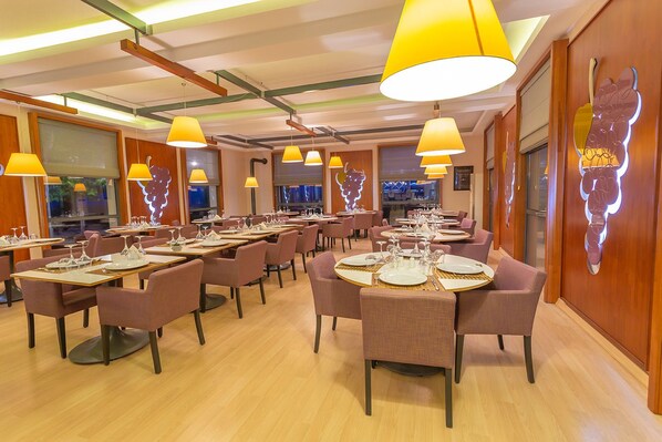 Un restaurante con mesas redondas, sillas rosadas y lámparas colgantes amarillas.