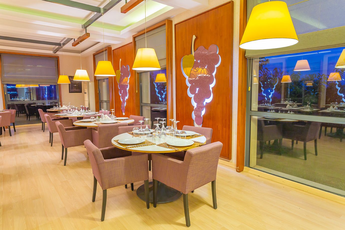 A modern restaurant with round tables, pink chairs, and yellow pendant lights.