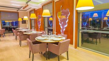 A modern restaurant with round tables, pink chairs, and yellow pendant lights.