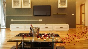 A modern living room with a flat-screen TV mounted on the wall, a glass coffee table with rose petals and glasses, and a fireplace with a metal bucket. - Hill Residence (Brasov)