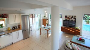 A modern kitchen with a stainless steel refrigerator, a dining area with a table set for two, and a living area with a sofa and a television. - Villa Villa Kos 19 Near Konnos Beach (Protaras)
