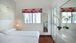 A bedroom with two beds, a large mirror, a window with shutters, and a bedside lamp. - Villa Villa Kos 19 Near Konnos Beach (Protaras)