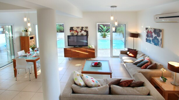 A modern living room with a sofa, coffee table, TV, and dining area. - Villa Villa Kos 19 Near Konnos Beach (Protaras)