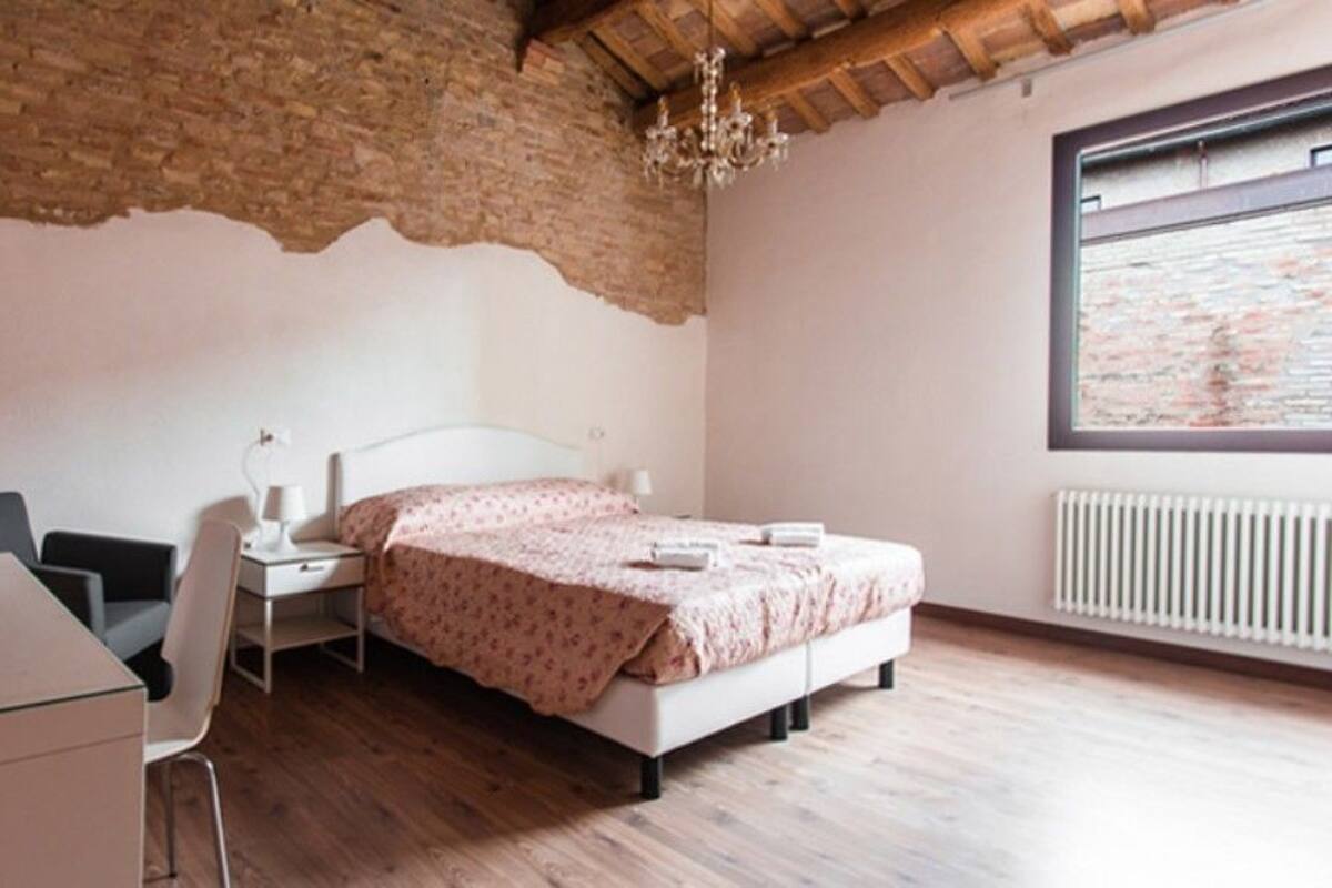 A bedroom with a bed, a desk, a chair, a radiator, and a window with a view.