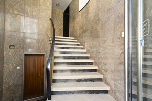 A marble staircase with a wooden door at the bottom and a glass elevator to the right.