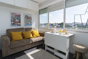A modern living room with a sofa, a small table with breakfast items, and a view of a cityscape through large windows. - Central Lisbon Apartment near Príncipe Real & Avenida da Liberdade - TTL308 (Lisboa ciudad)