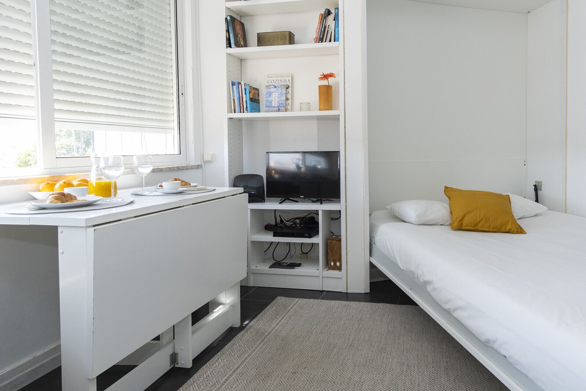A bedroom with a bed, a white desk with a television, and a bookshelf.