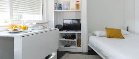 Un dormitorio con cama, un escritorio blanco con televisor y una estantería.