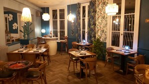 A restaurant interior with wooden furniture, hanging lights, and large windows with curtains. - Hotel Restaurant L'Escapade (Carentan les Marais)