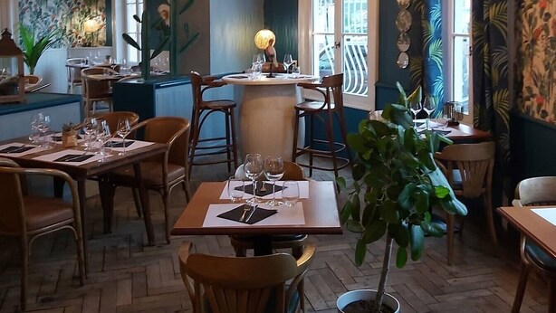 A restaurant interior with wooden furniture, hanging pendant lights, and tropical-themed curtains. - Hotel Restaurant L'Escapade (Carentan les Marais)