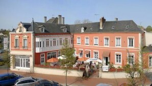 A red brick building with a corner entrance, a small outdoor seating area, and a visible storefront. - Hotel Restaurant L'Escapade (Carentan les Marais)