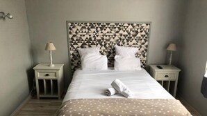A neatly made bed with a patterned headboard, two bedside tables with lamps, and a polka-dotted throw blanket. - Hotel Restaurant L'Escapade (Carentan les Marais)