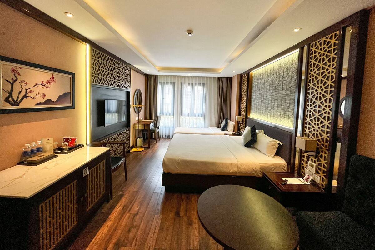 A hotel room with a bed, desk, chair, TV, and decorative screens.