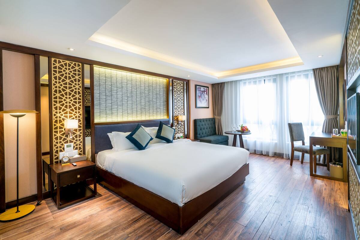 A hotel room with a large bed, a desk, a chair, a TV, and a window with curtains.