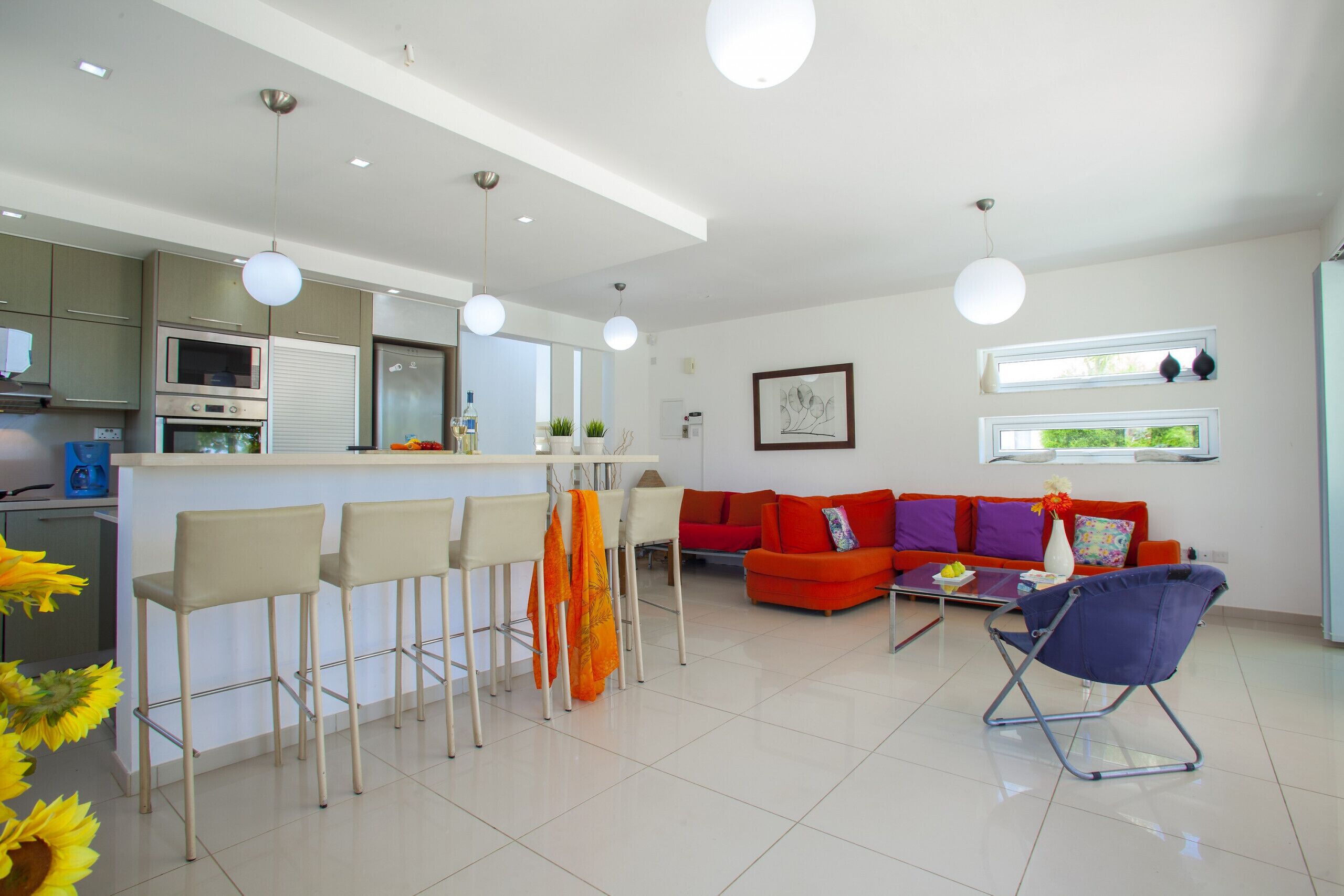 Een moderne keuken met barstoelen, een rode bank en een blauwe stoel.