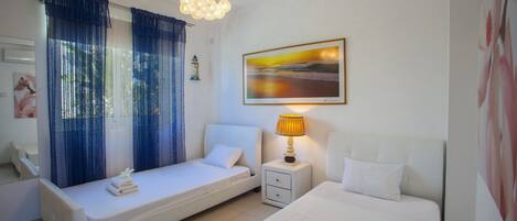 Een hotelkamer met een bed, een slaapbank, een nachtkastje met een lamp, een schilderij aan de muur en een raam met gordijnen.