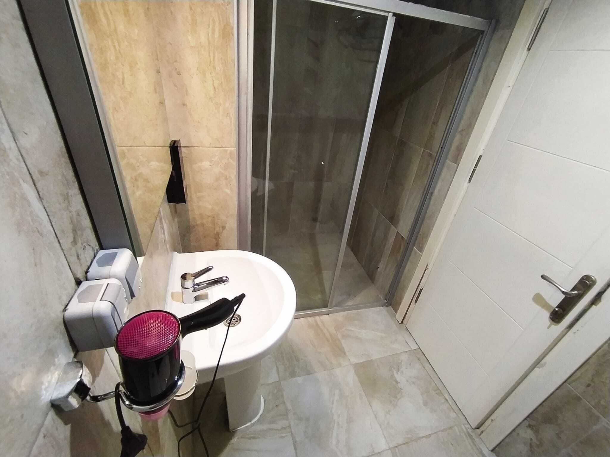 Un baño con lavamanos blanco, espejo y cabina de ducha.