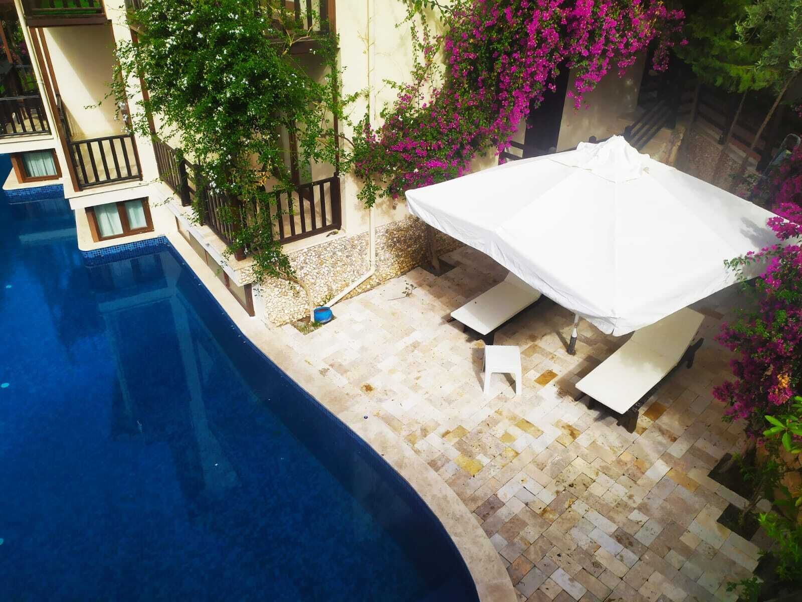 A swimming pool area with a tiled deck, a white umbrella, and potted plants.