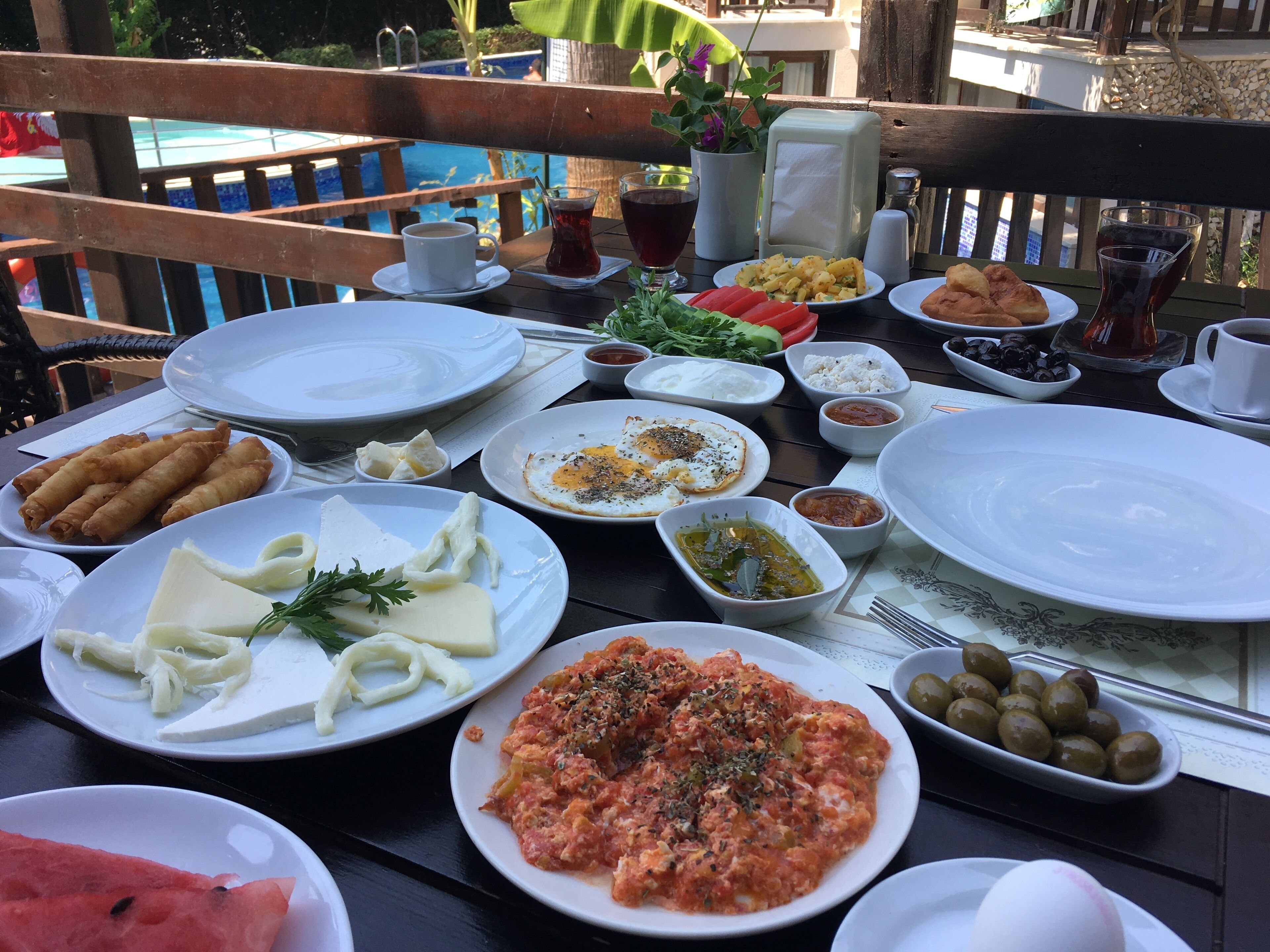 Een tafel gedekt met verschillende gerechten, zoals pasta, eieren en salades, met een zwembad op de achtergrond.