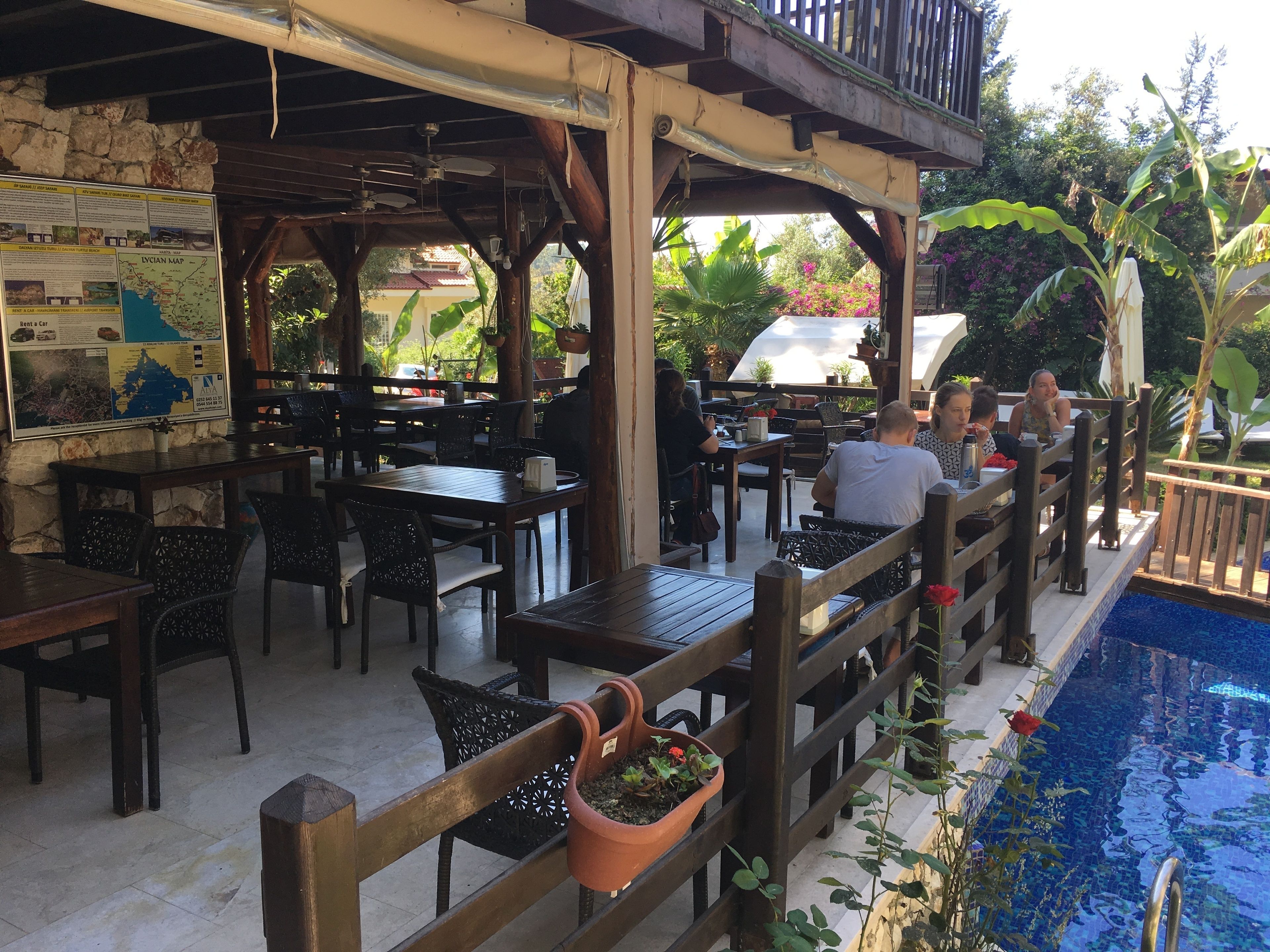 An outdoor dining area with wooden tables and chairs, a pool, and a map on the wall.