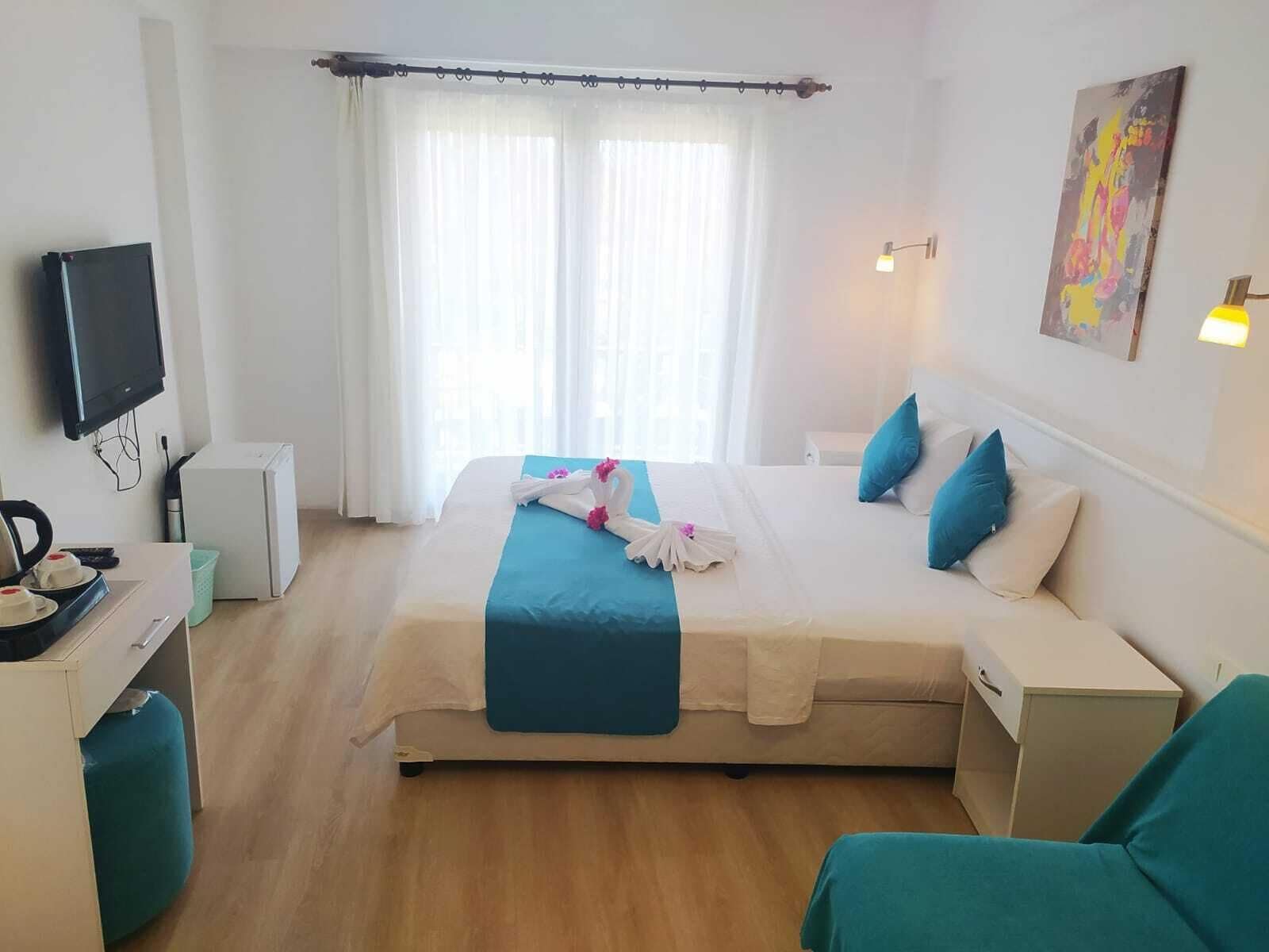 Quarto de hotel com cama, escrivaninha, televisão e janela com cortinas.