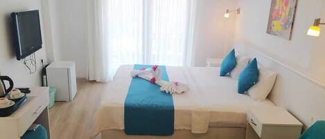 Quarto de hotel com cama, escrivaninha, televisão e janela com cortinas.