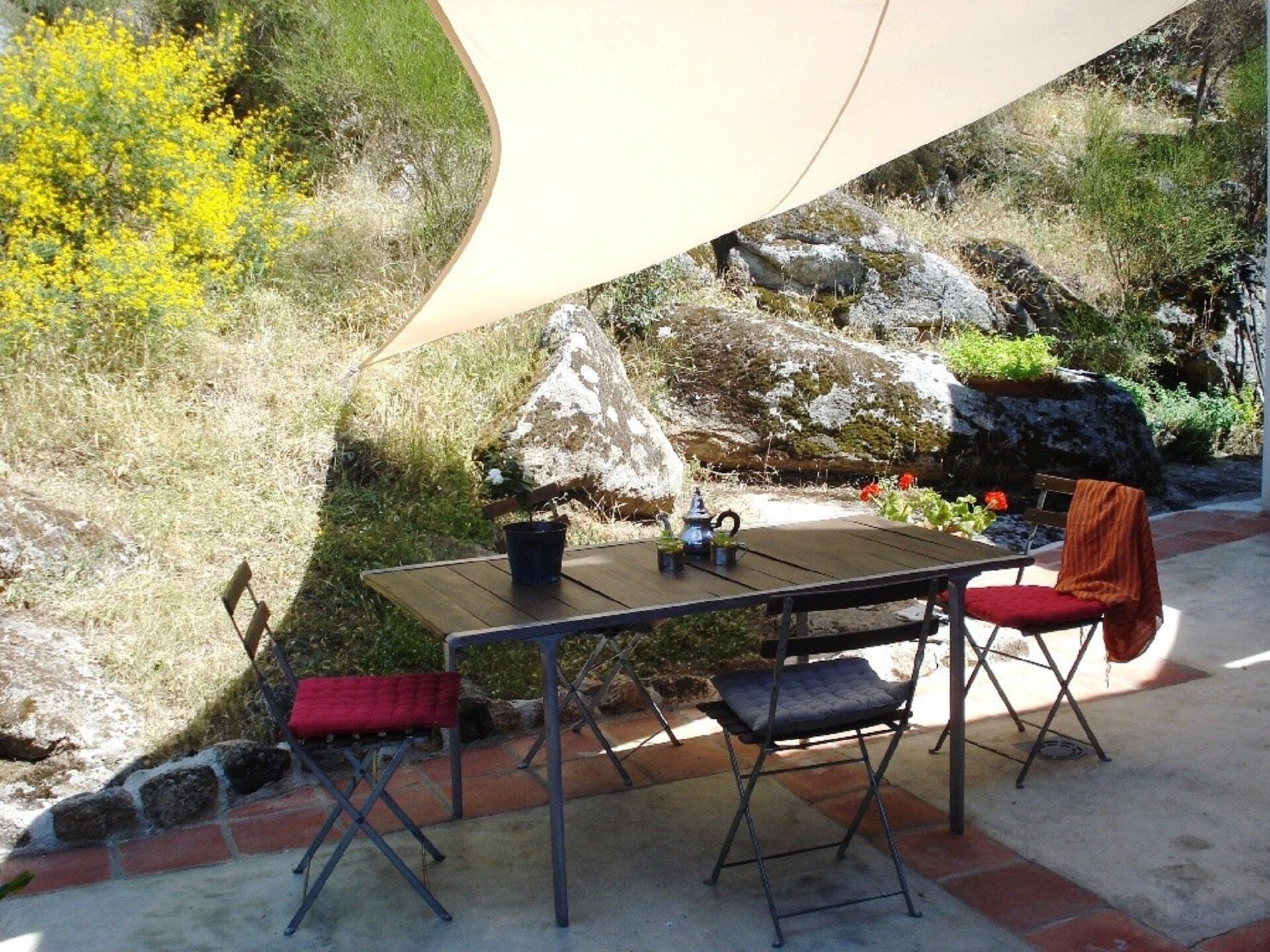 Un área de comedor al aire libre con una mesa, sillas, una planta en maceta y una formación rocosa al fondo.