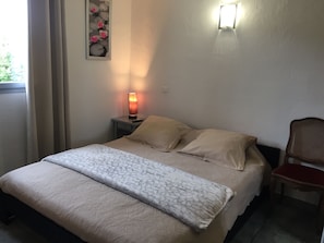 A neatly made bed with a patterned bedspread and pillows, a bedside lamp, a chair, and a wall-mounted light fixture.