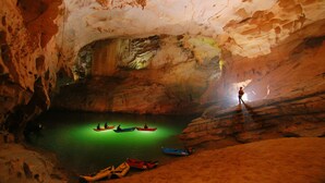 Una cueva con barcos en el agua y una persona de pie en un saliente.