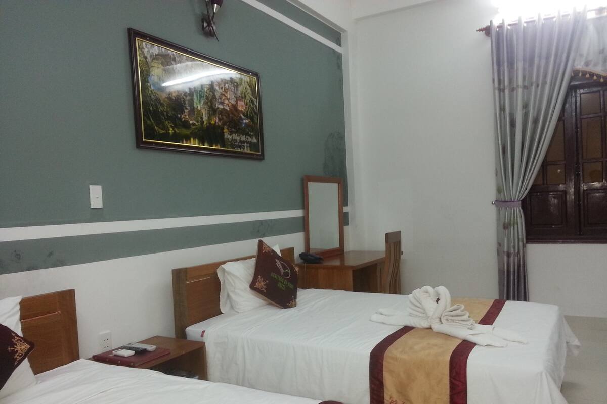 Quarto de hotel com duas camas, uma escrivaninha, uma cadeira, um espelho e um quadro na parede.