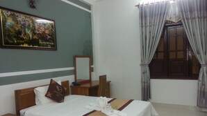 Una habitación de hotel con una cama, una mesita de noche, una silla de madera, un escritorio, un espejo y una ventana con cortinas.