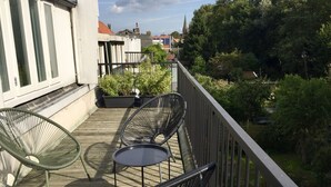Un balcó amb dues cadires i una taula petita, envoltat de plantes en testos i vista a un jardí.