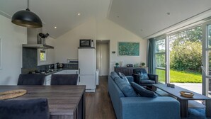A modern kitchen with a dining area, a living room with a sofa and coffee table, and a large sliding glass door to a garden.
