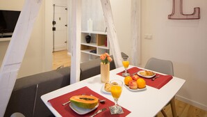 A dining area with a table set for breakfast, including a plate of fruit, a glass of orange juice, and a croissant.
