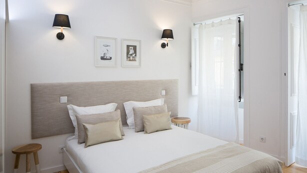 A bedroom with a large bed, two wall-mounted lamps, a small stool, and a door with a curtain.