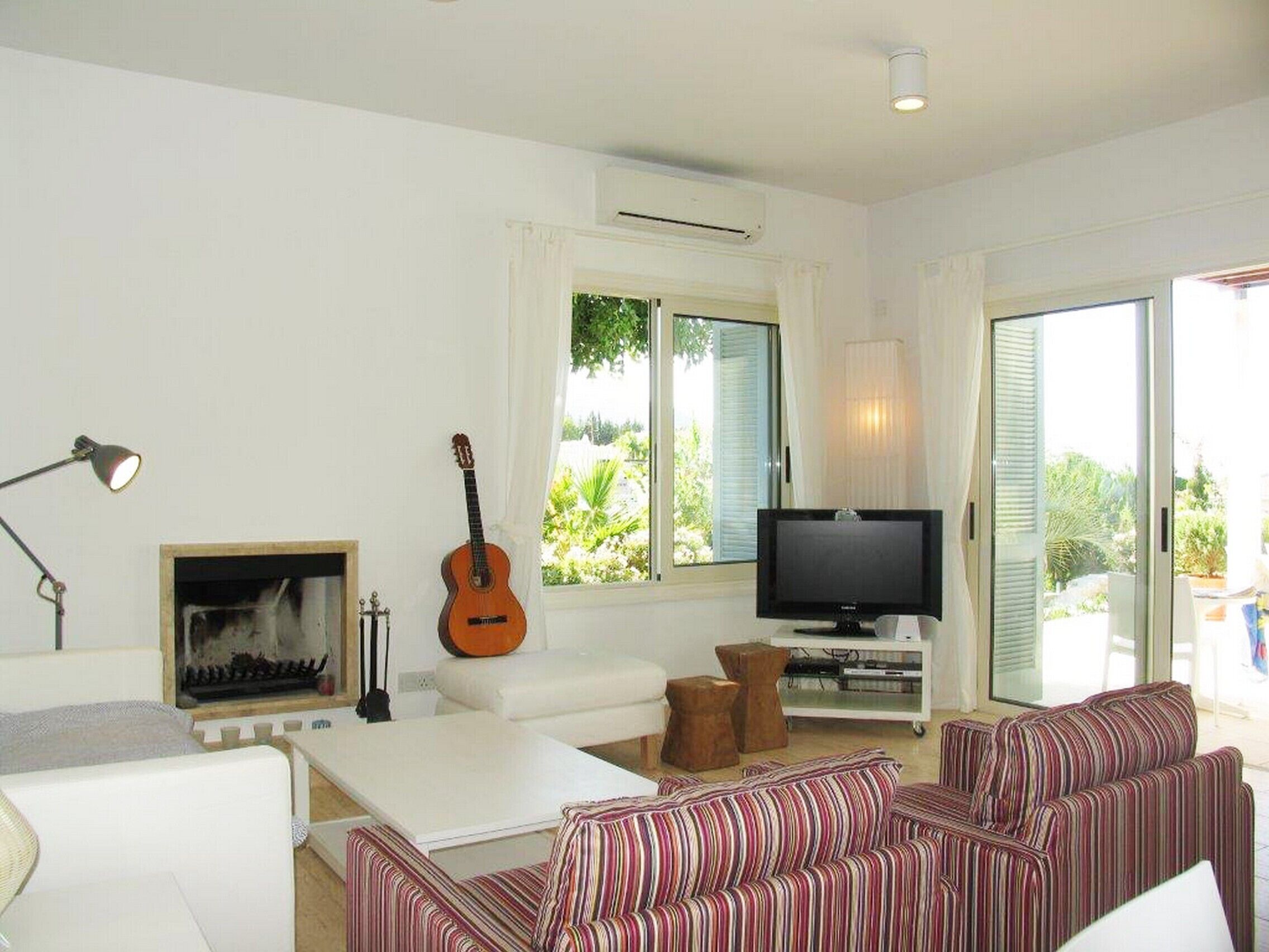 A living room with a white sofa, a striped couch, a guitar, a TV, and a fireplace.
