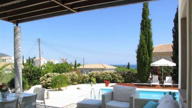 A covered outdoor area with wicker furniture, a pool, and a view of the sea. - Carob Tree villa near The Centre (Latsi)