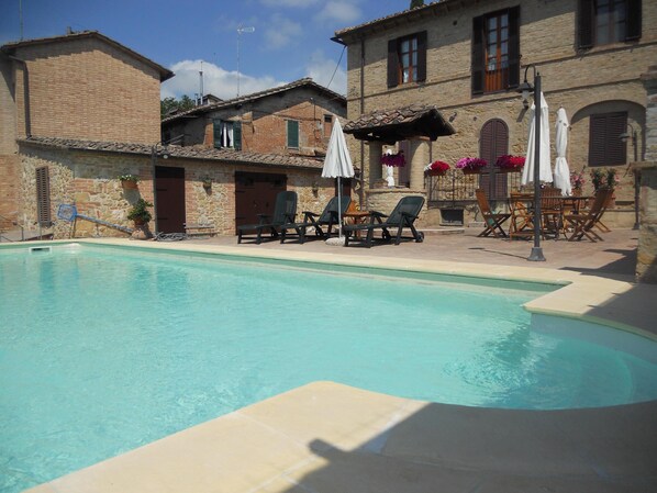 A swimming pool with lounge chairs and umbrellas, surrounded by stone buildings with windows and shutters. - Apartment in a farmhouse a few km from the center (Siena)