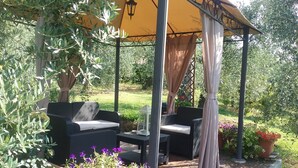 Ulkoterassi, jossa on rottinkihuonekaluja, pergola, jonka yllä on keltainen katos, sekä ruukkukasveja.