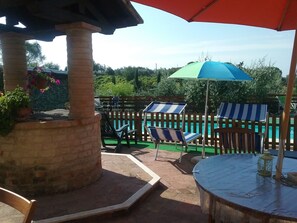A poolside area with lounge chairs, a table, and a pergola with a hanging flower pot. - Apartment in a farmhouse a few km from the center (Siena)