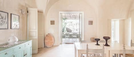 Una habitación amplia con un techo alto y arqueado, una zona de comedor con una mesa y sillas, y un jarrón grande sobre un mueble.