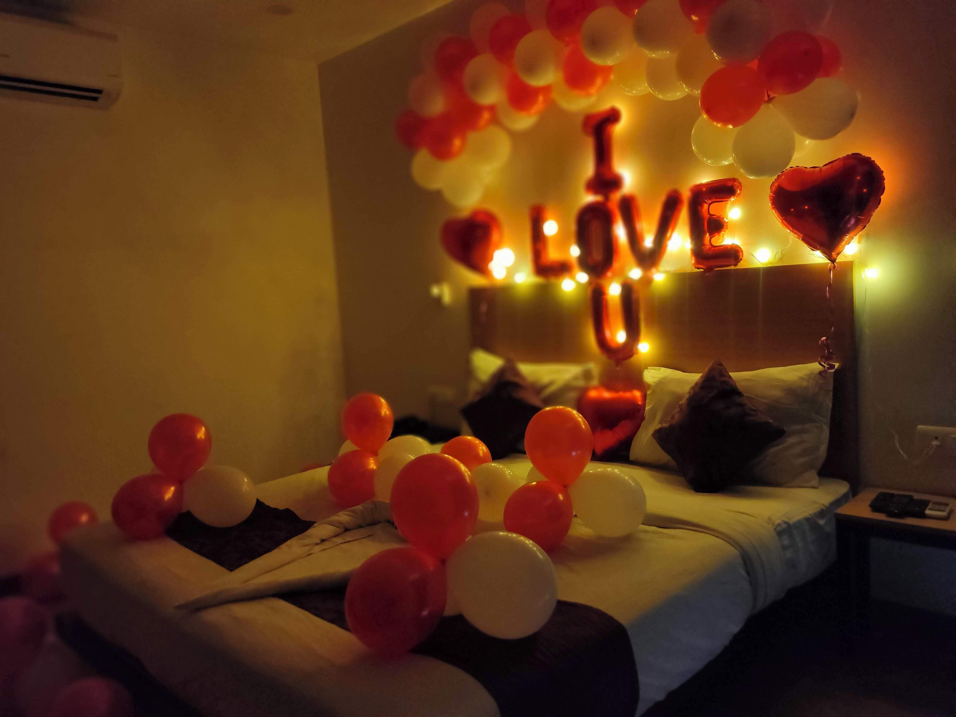 A bedroom with a bed, pillows, and a string of balloons spelling "LOVE" in the background.