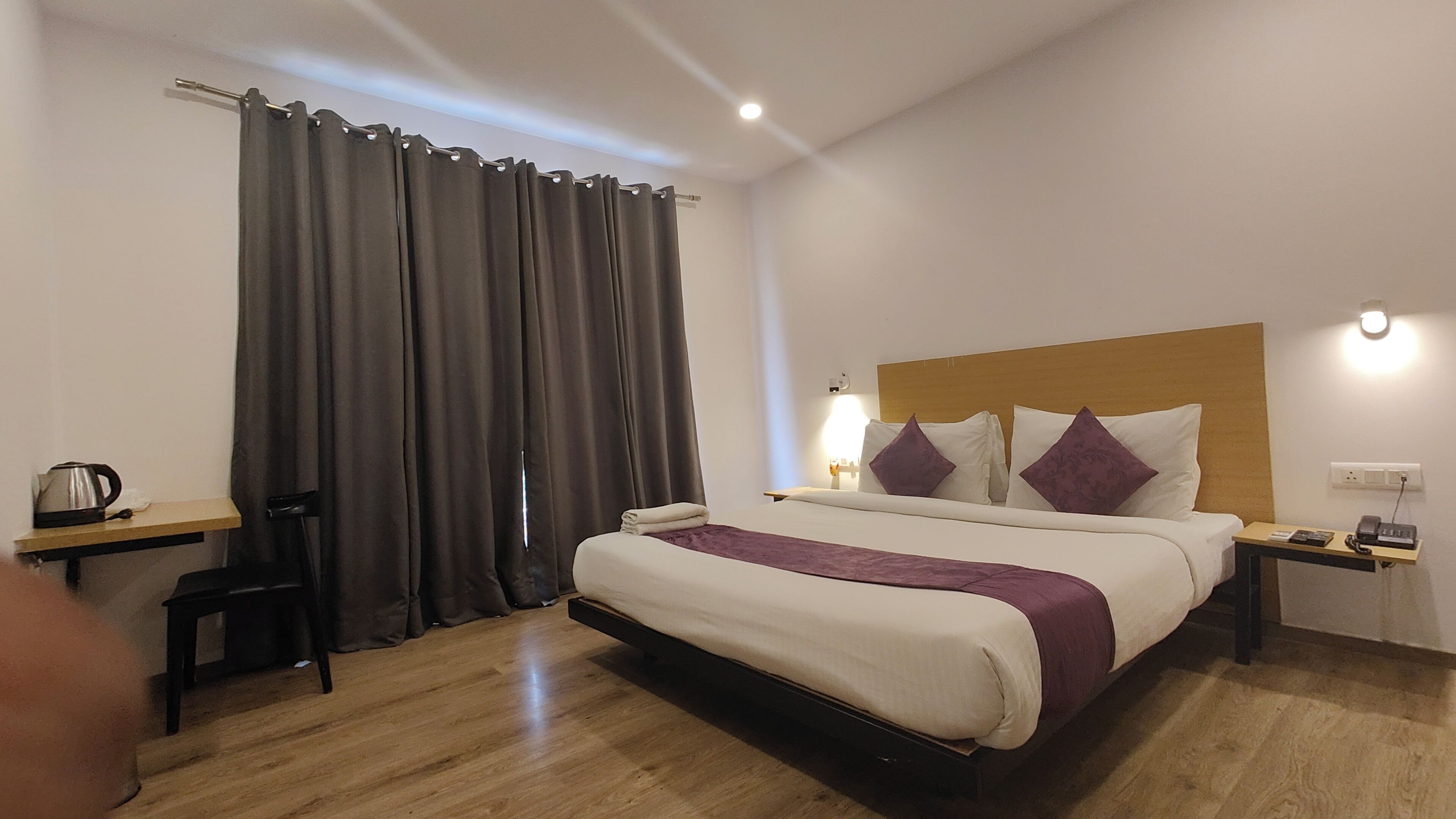 A hotel room with a bed, bedside tables, a desk, a chair, a coffee maker, and a curtain.