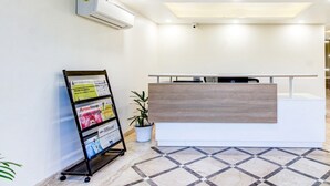 A reception area with a reception desk, a wall-mounted air conditioner, a bulletin board with various notices, and a potted plant.