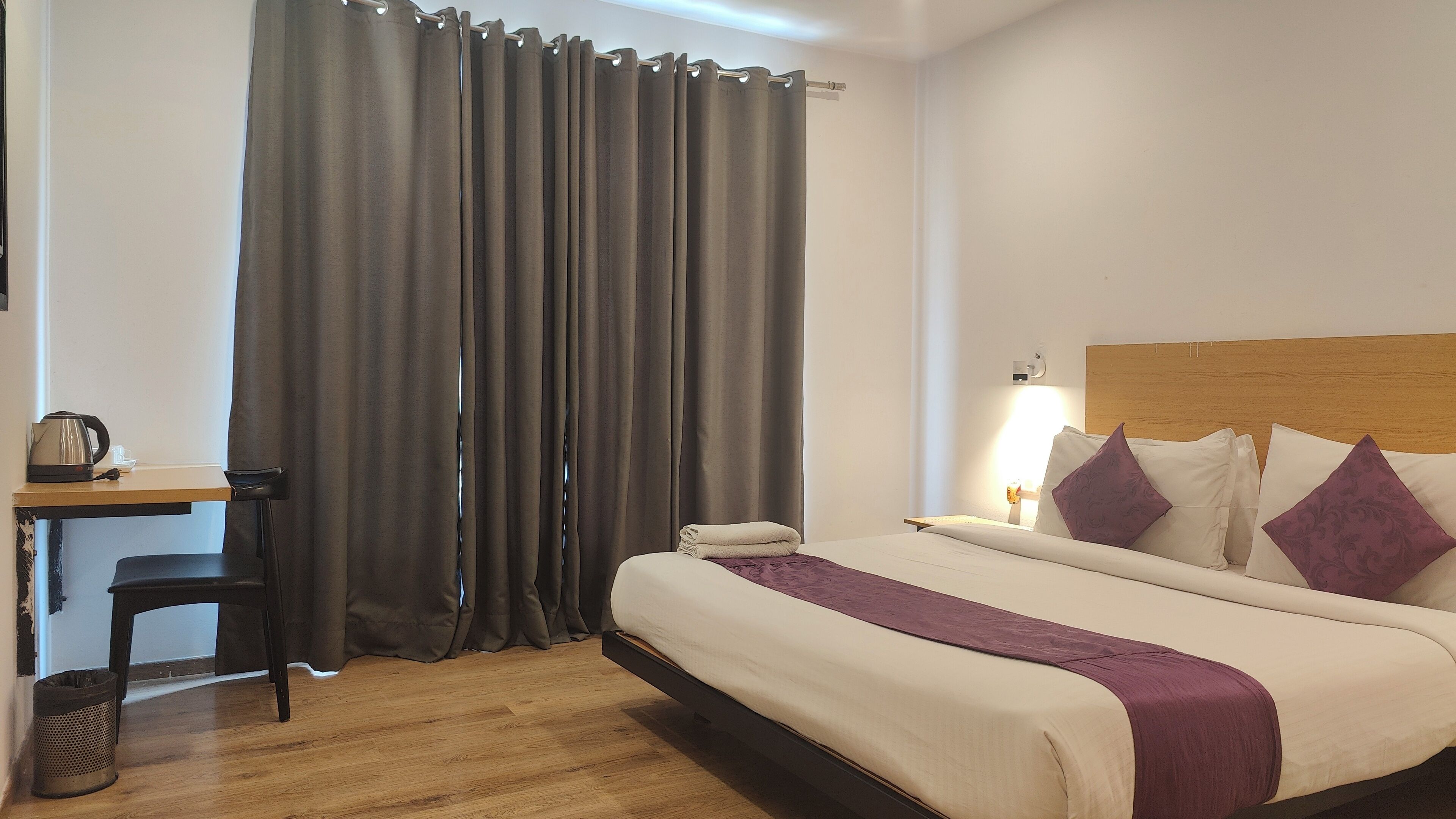 A hotel room with a bed, a desk, a chair, a lamp, and a curtain.