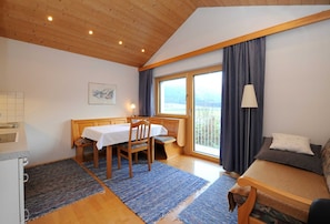 Ein Zimmer mit Holzboden, einem Esstisch mit Stühlen, einer Couch, einem Fenster mit Vorhängen und einer Lampe.