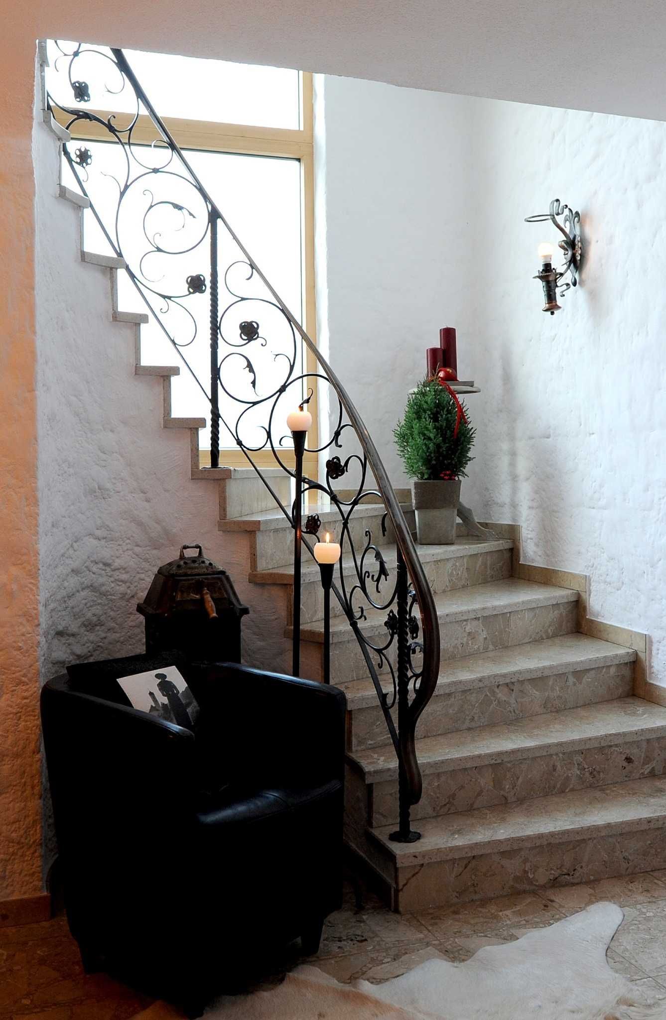 Eine Treppe mit aufwendiger Metallreling, einem kleinen Topfpflanzen und einer Wandleuchte.