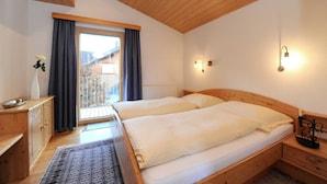 Une chambre avec deux lits, un plafond en bois, une fenêtre avec des rideaux, une table de chevet et une petite table.