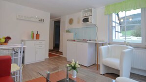 Una cocina moderna con armarios blancos, un microondas y una zona de comedor con una silla roja y una mesa de vidrio.