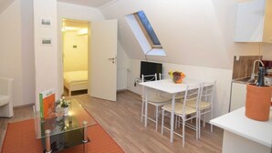 Una habitación moderna y bien iluminada con una mesa de vidrio, sillas blancas, una pequeña cocina y un tragaluz.
